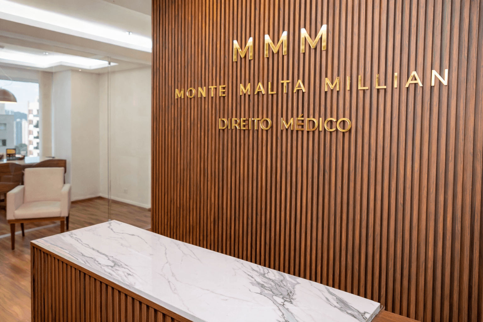 Recepção do escritório MMM Direito Médico com logo dourado na parede de madeira e mesa de mármore